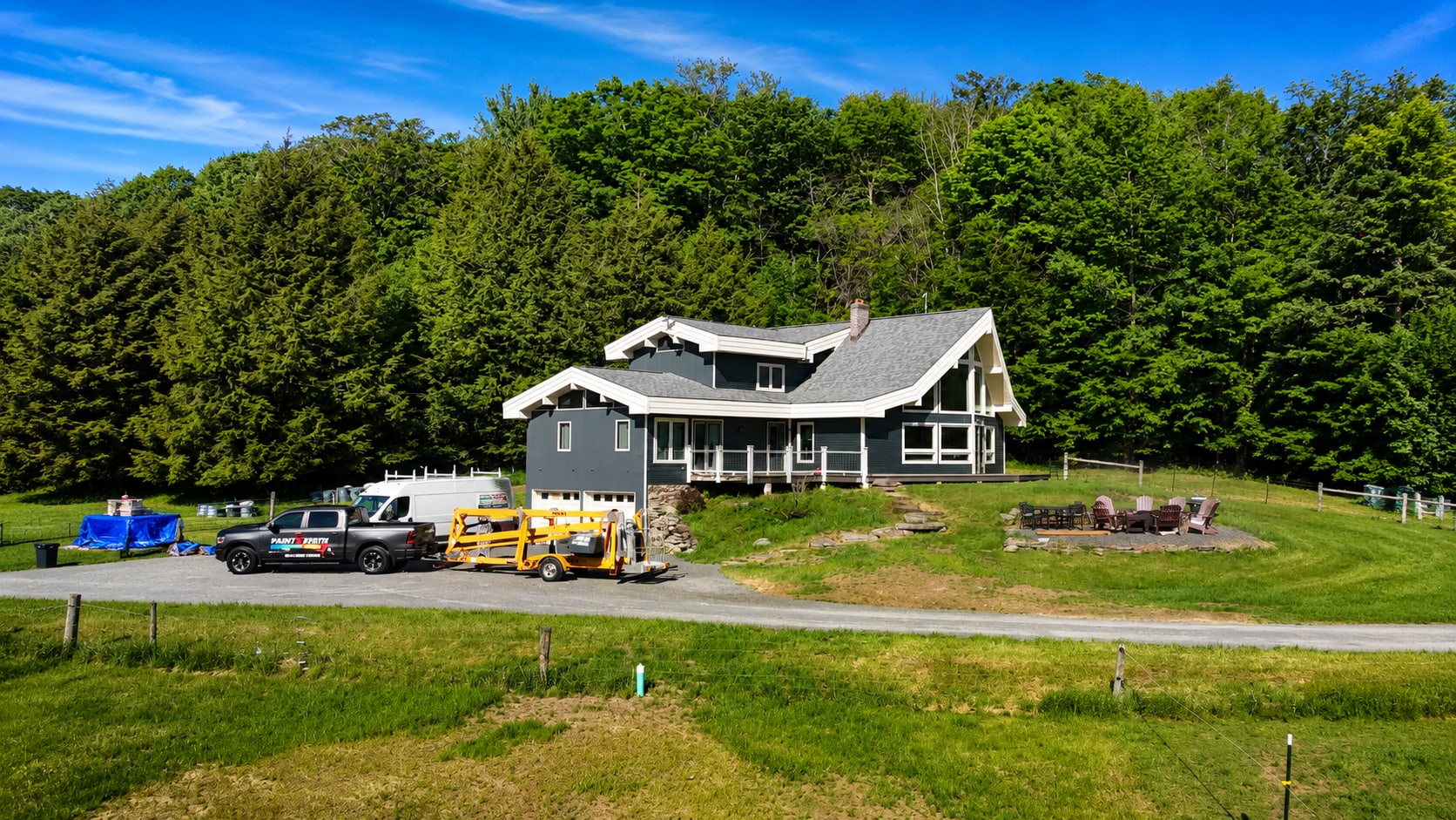 Lift and crew vehicles on site for an exterior repaint on a hillside house