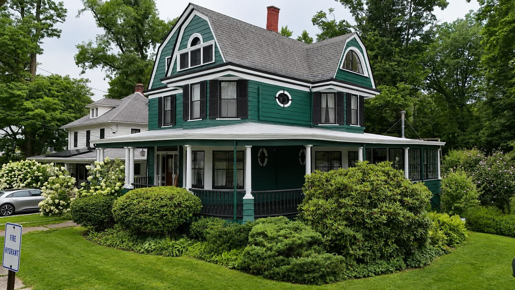 Green Victorian with a gambrel roof and wraparound porch, the white trim and spindle detail picked out by hand