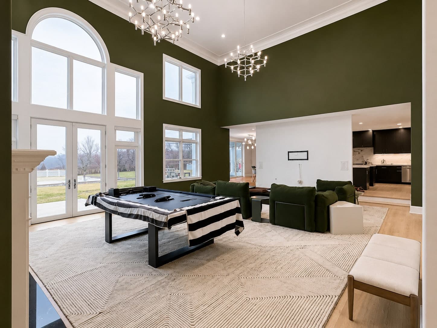 Double-height great room finished in a deep green with white trim and a wall of tall windows